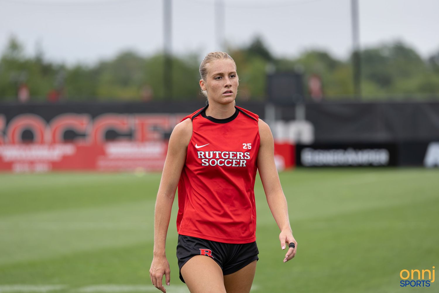 Female Rutgers Soccer player in red uniform training on green field during outdoor practice session.