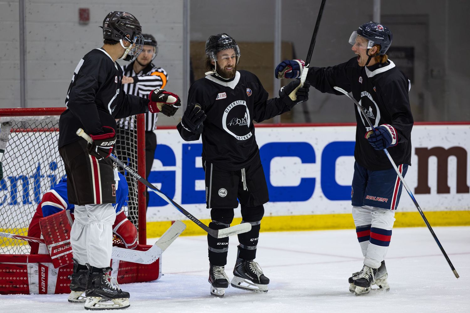 Ice hockey players celebrate on the rink during a practice session, wearing black and blue jerseys in an indoor arena.