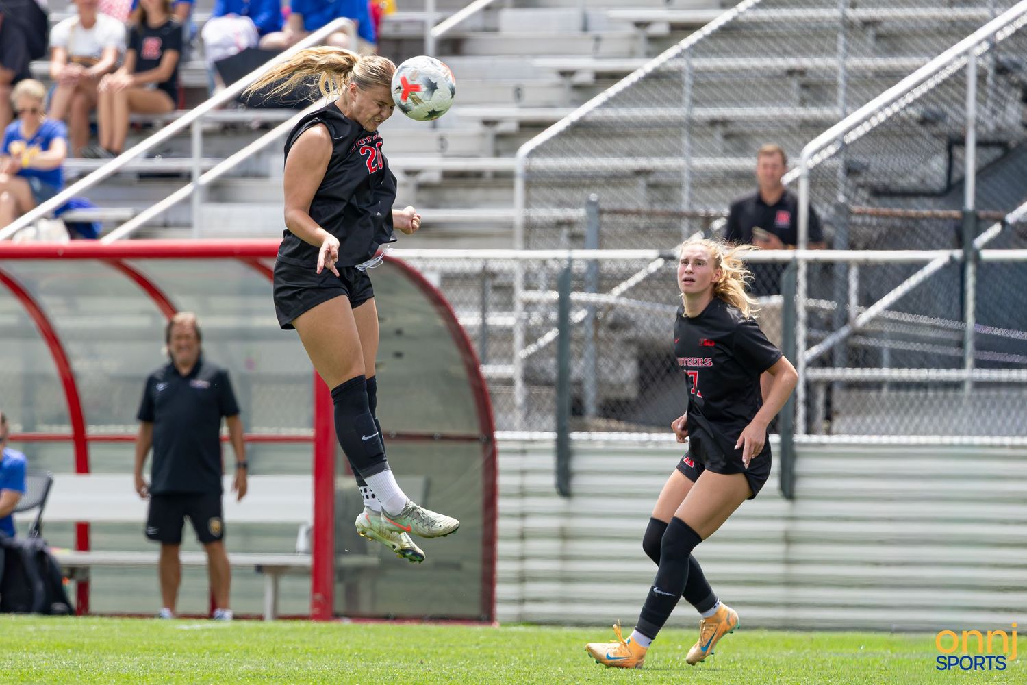 Female soccer player heads the ball mid-air during a competitive match, with teammate watching nearby.