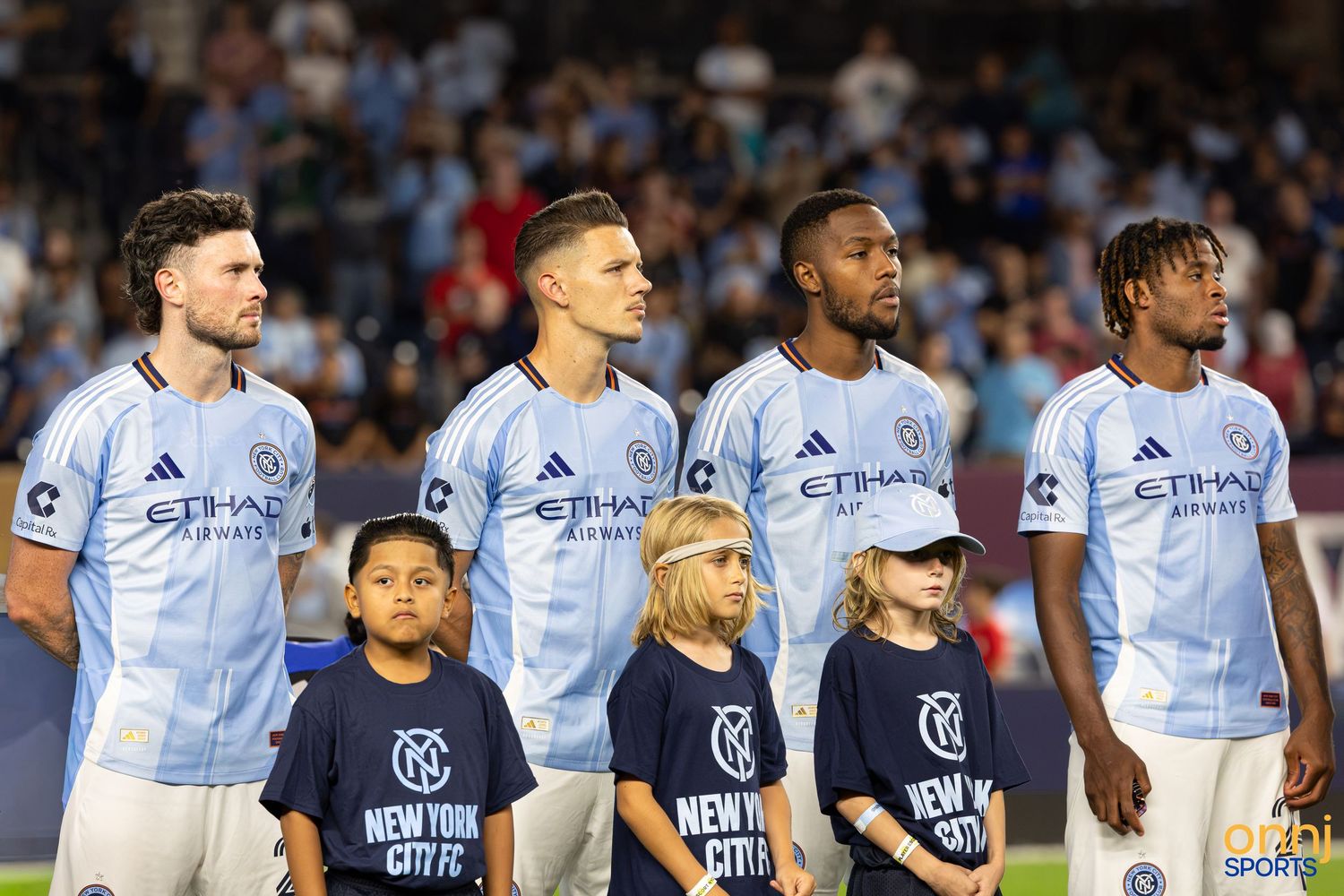 NYCFC players line up with young mascots in light blue Etihad-sponsored jerseys during an MLS match.
