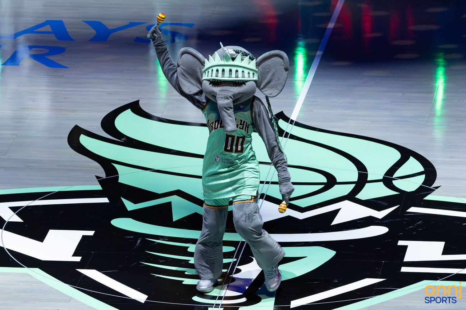 NBA mascot elephant costume performing on court during game, wearing teal jersey and Statue of Liberty crown.