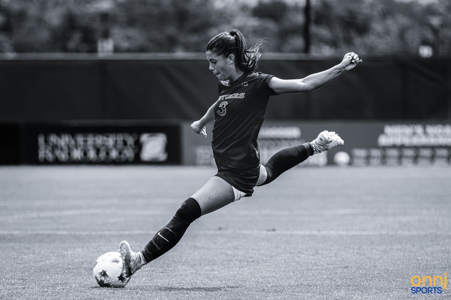 Female soccer player in black uniform kicking ball on field during a competitive match.