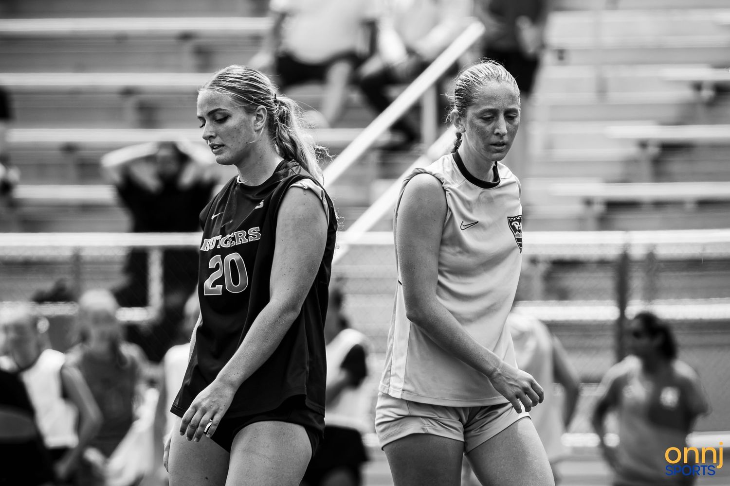 Two female athletes in black and white photo wearing jerseys numbered 20 during an outdoor sports event.