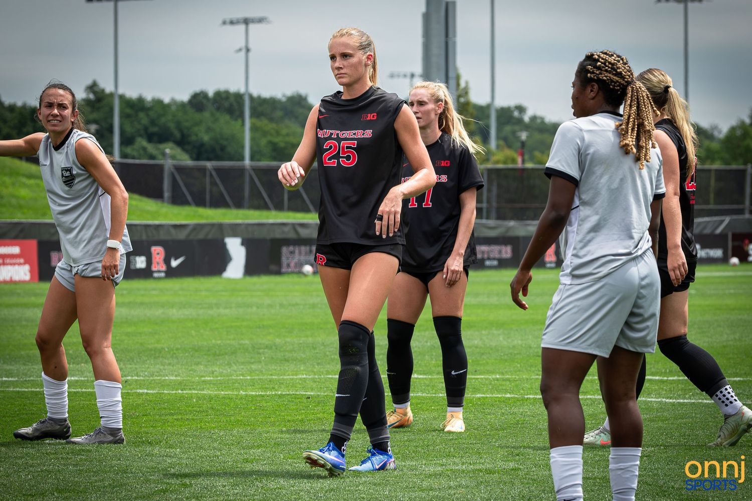 Women's college soccer players in red uniforms on green field during a game, player #25 prominent.