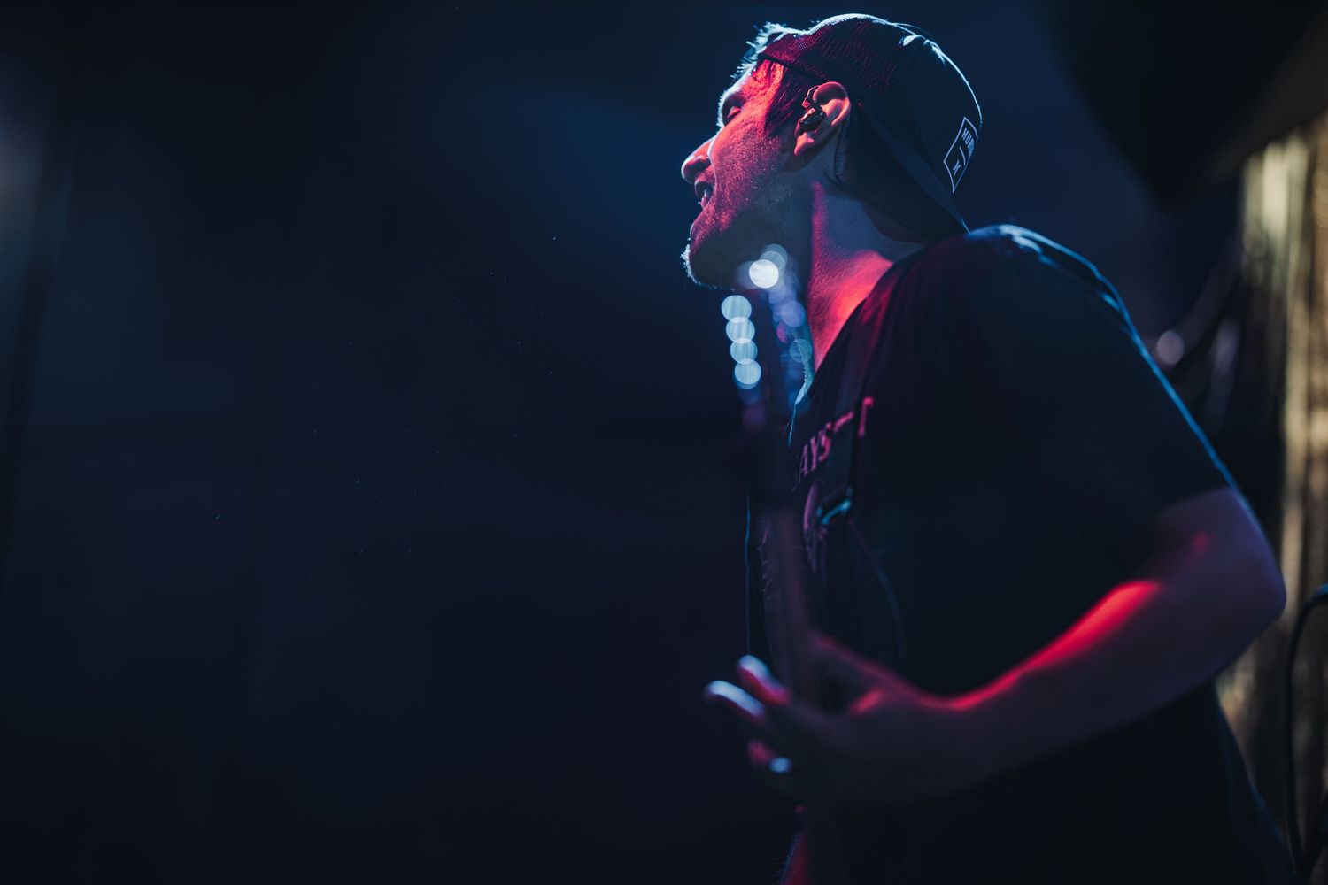 Male singer performing on stage under dramatic red and blue lighting in a dark concert venue.
