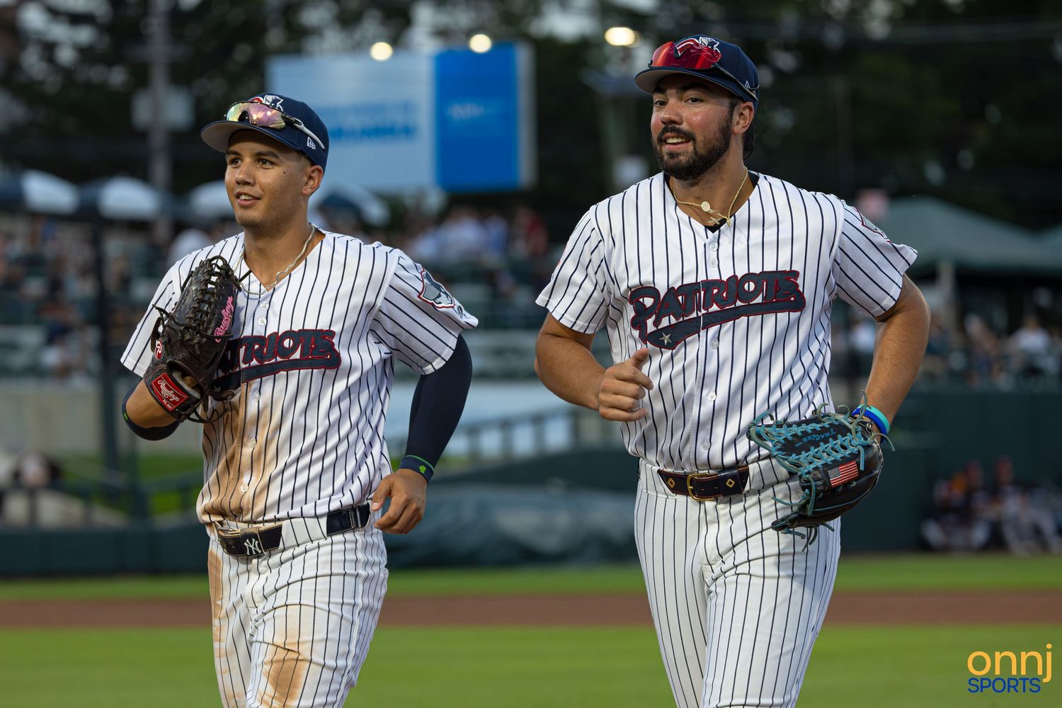 Two baseball players in pinstripe uniforms jogging on the field during a night game.