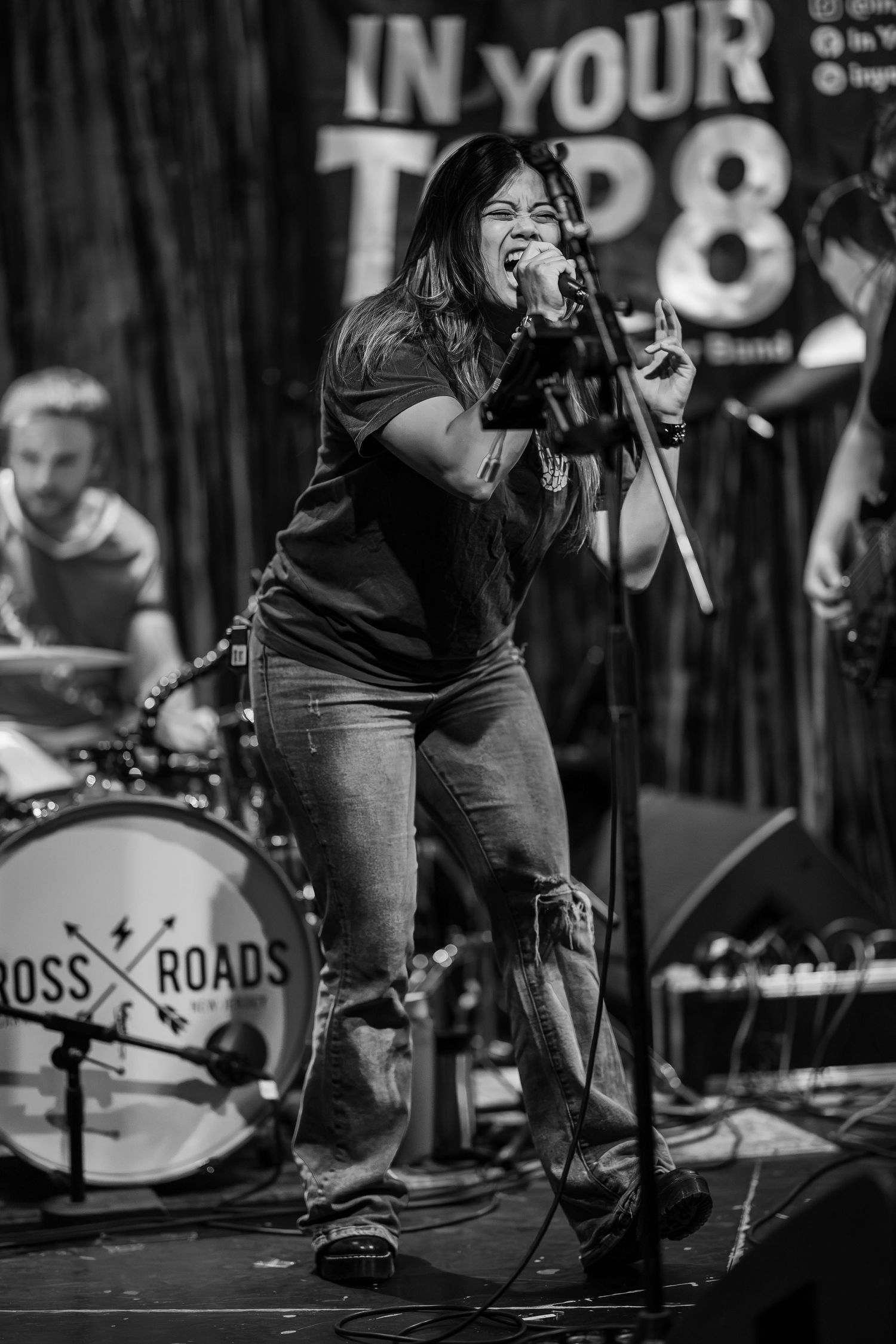 Black and white photo of a female vocalist performing on stage with a band at Crossroads venue.