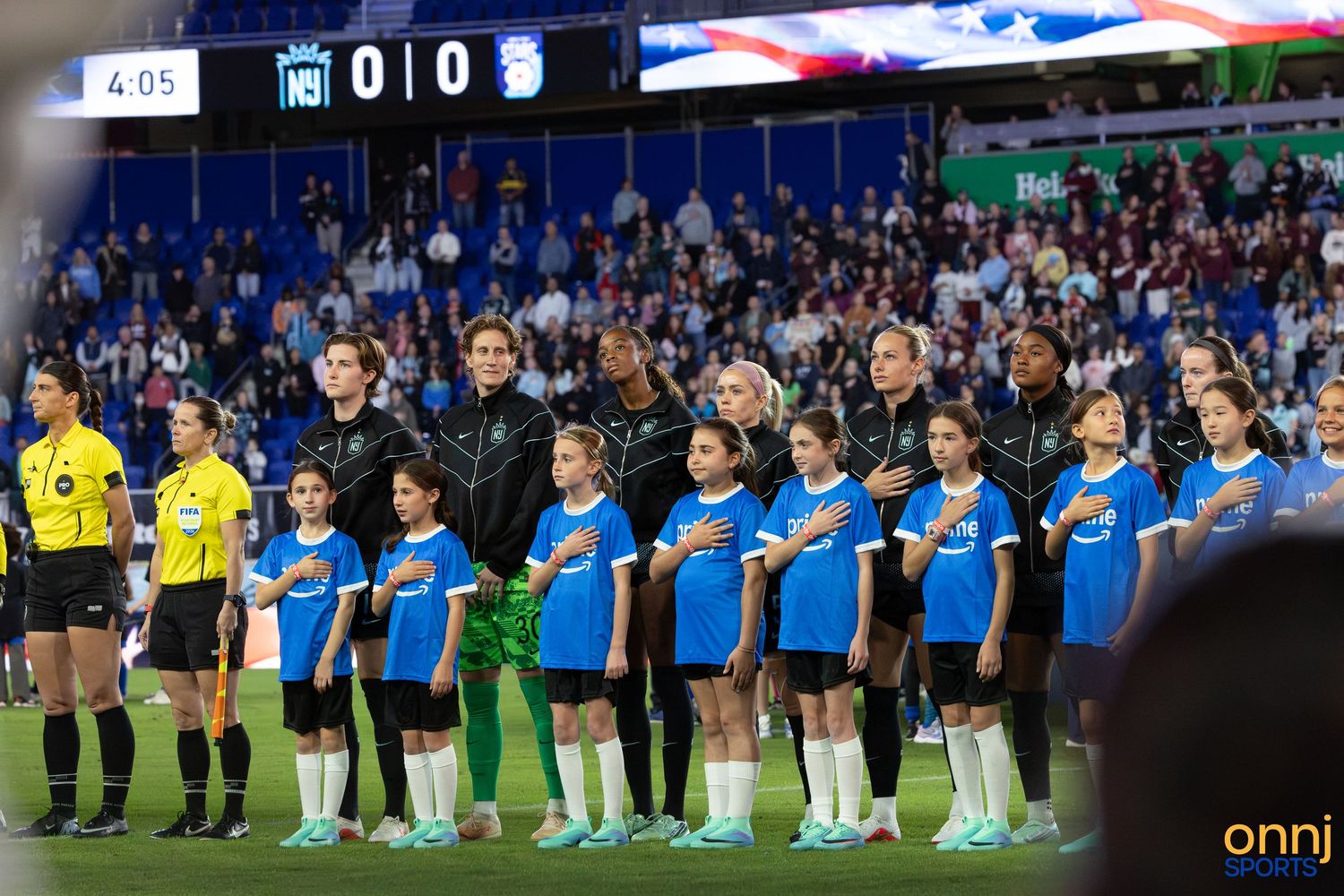Women's soccer team lines up with young fans during national anthem at professional match.