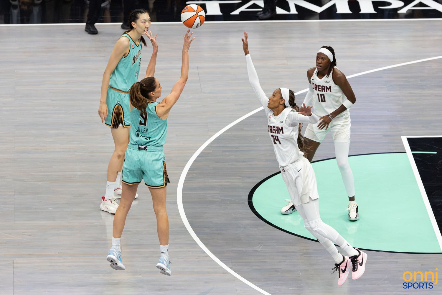 WNBA players compete during a game, with one athlete shooting over defenders near the Tampa arena baseline.