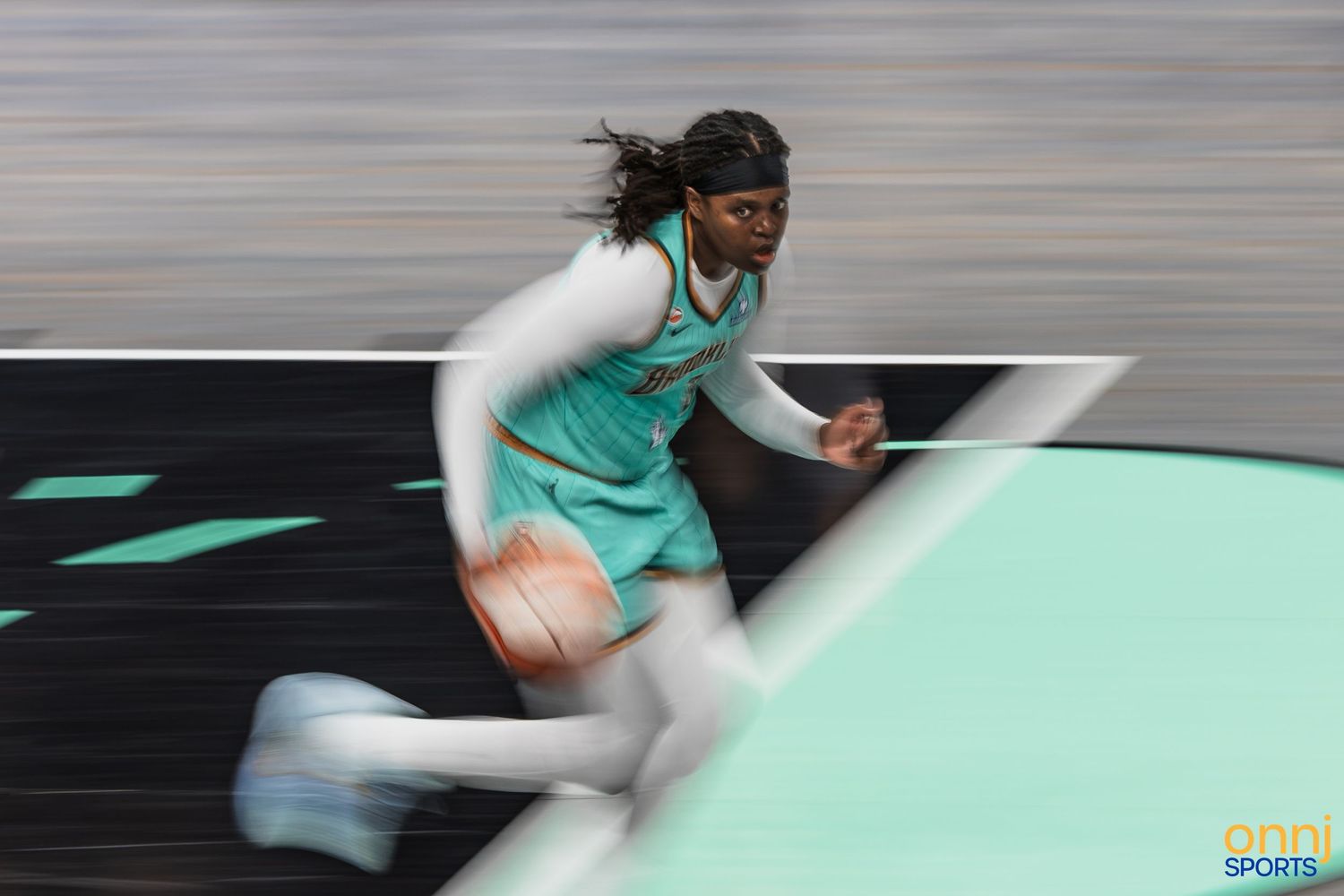 WNBA player dribbling basketball at full speed on teal court in action shot.