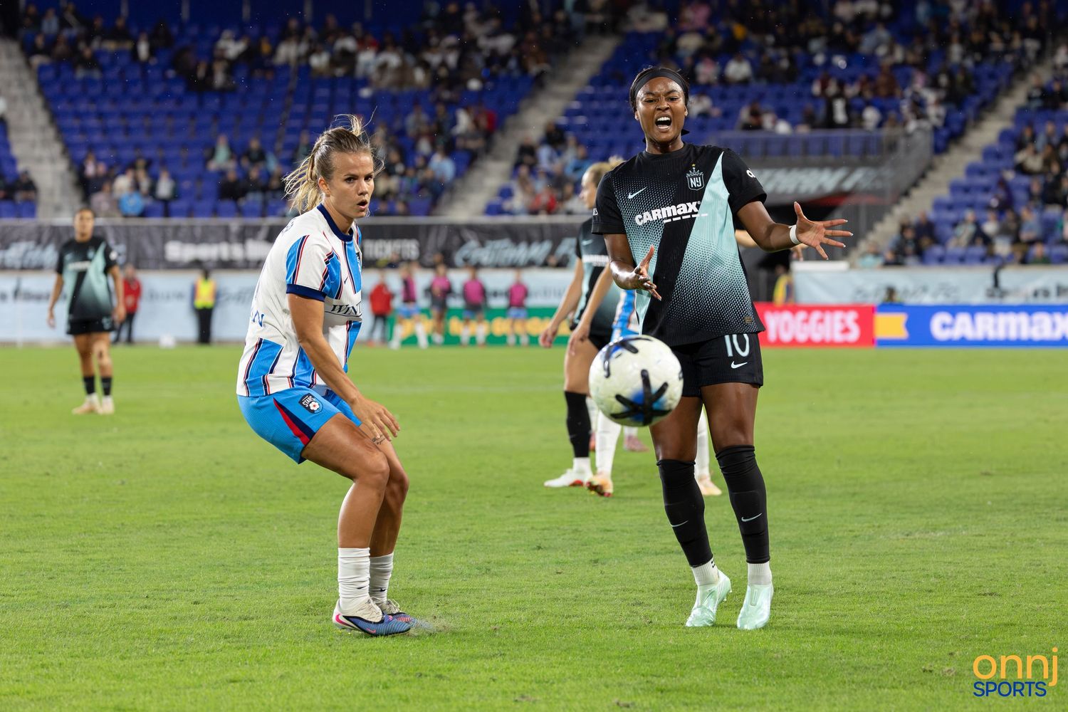 Two female soccer players compete for the ball during a professional match, one in white and one in dark uniform.