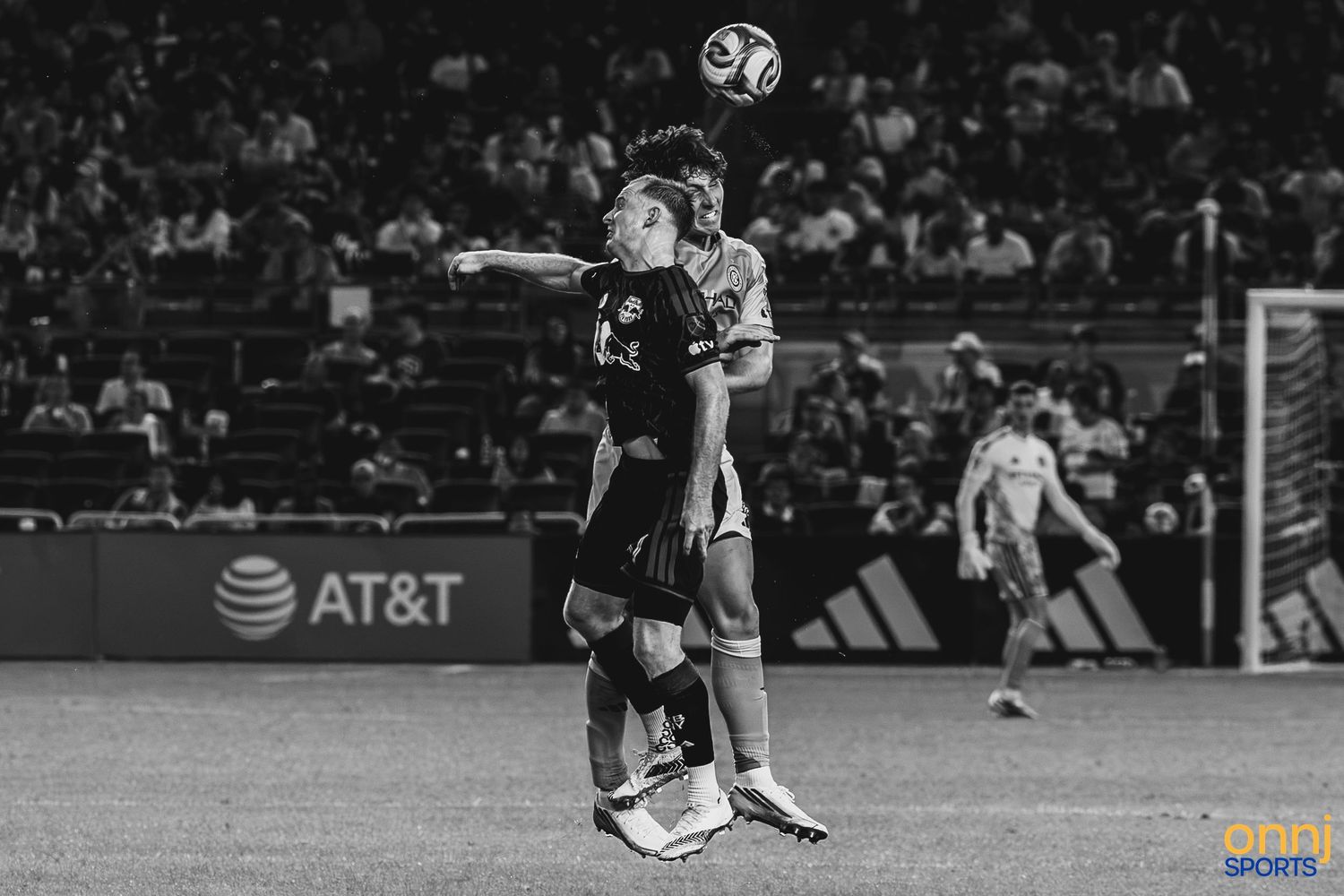 Two soccer players compete for a header during an MLS night match, captured in dramatic black and white photography.