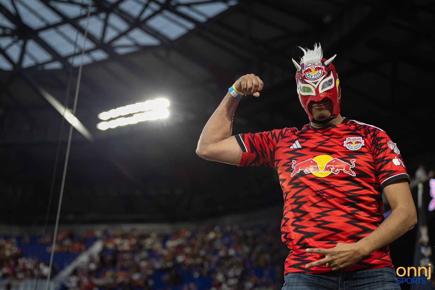 New York Red Bulls fan flexing in a lucha libre mask at Red Bull Arena during an MLS match.