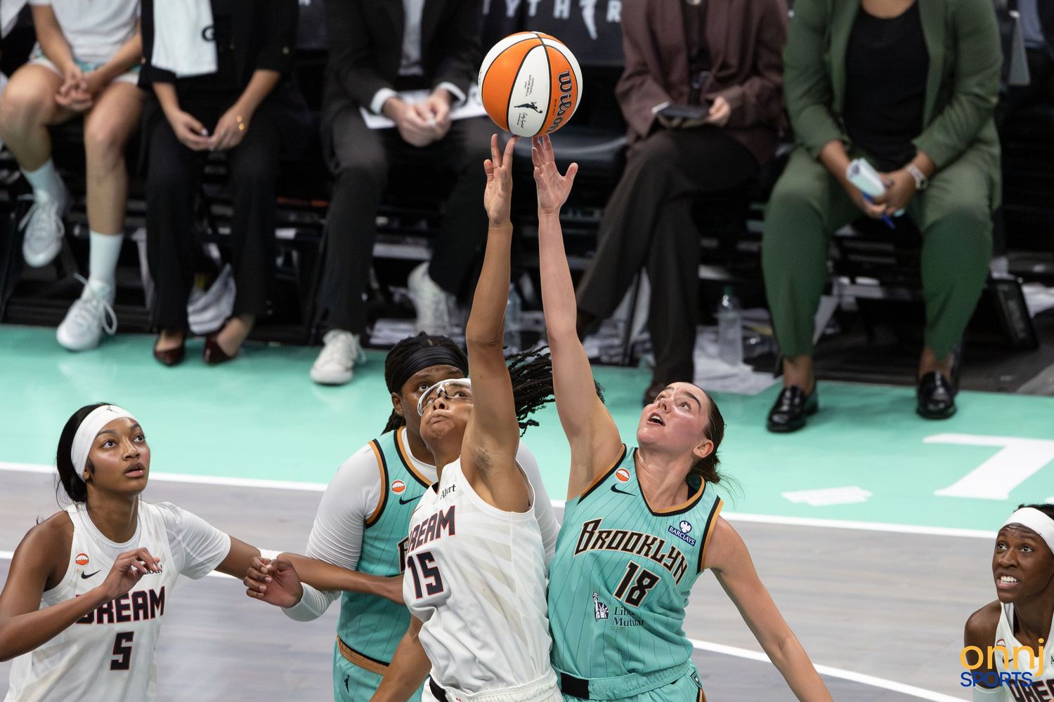 WNBA players from Atlanta Dream and Brooklyn compete for a rebound during an intense basketball game.