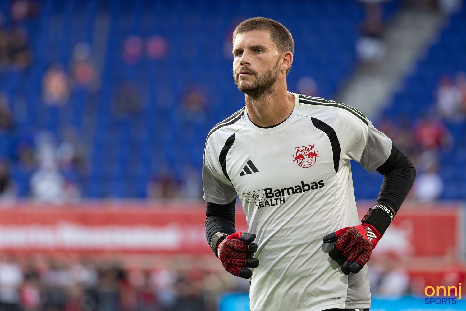New York Red Bulls goalkeeper in gray jersey and red gloves stands on field during MLS match warmup.