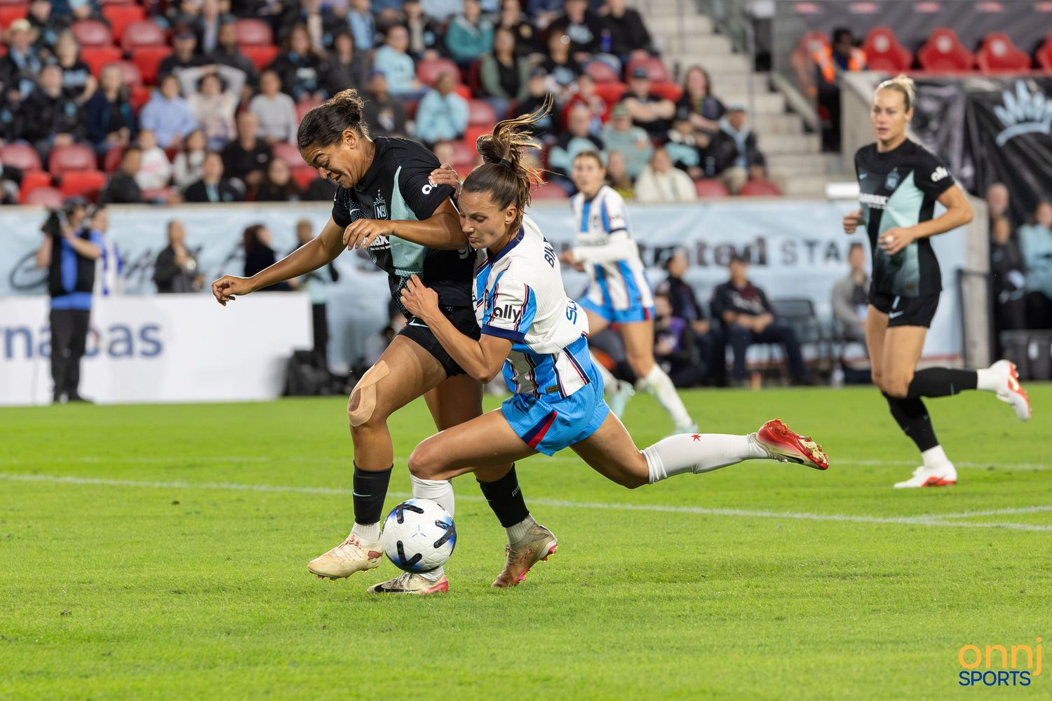 Two female soccer players compete for the ball during a professional women's football match on a stadium pitch.
