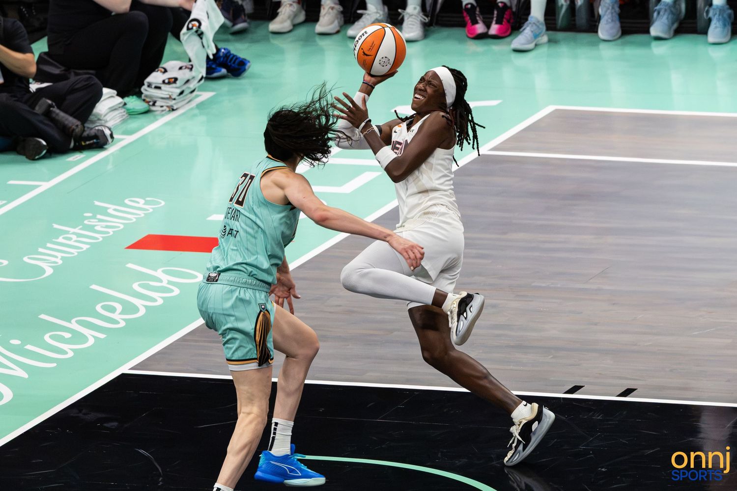 WNBA player drives to the basket past a defender during an indoor basketball game on a teal court.
