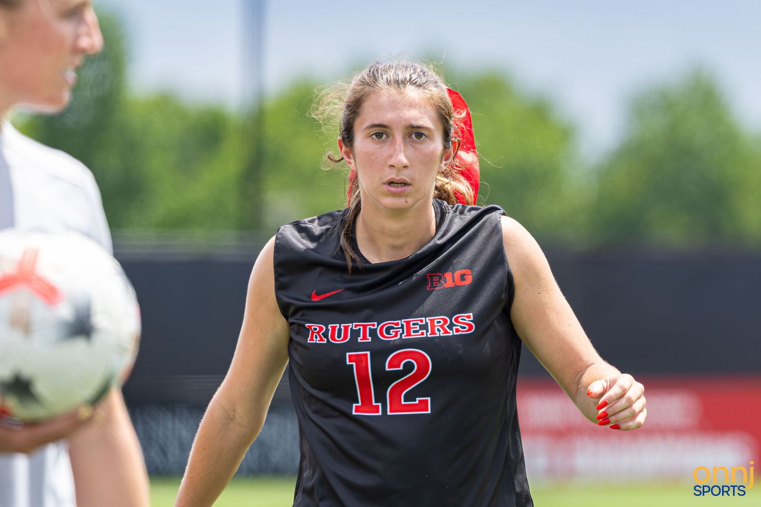 Rutgers women's soccer player #12 in black jersey focuses during an outdoor practice session on a sunny day.