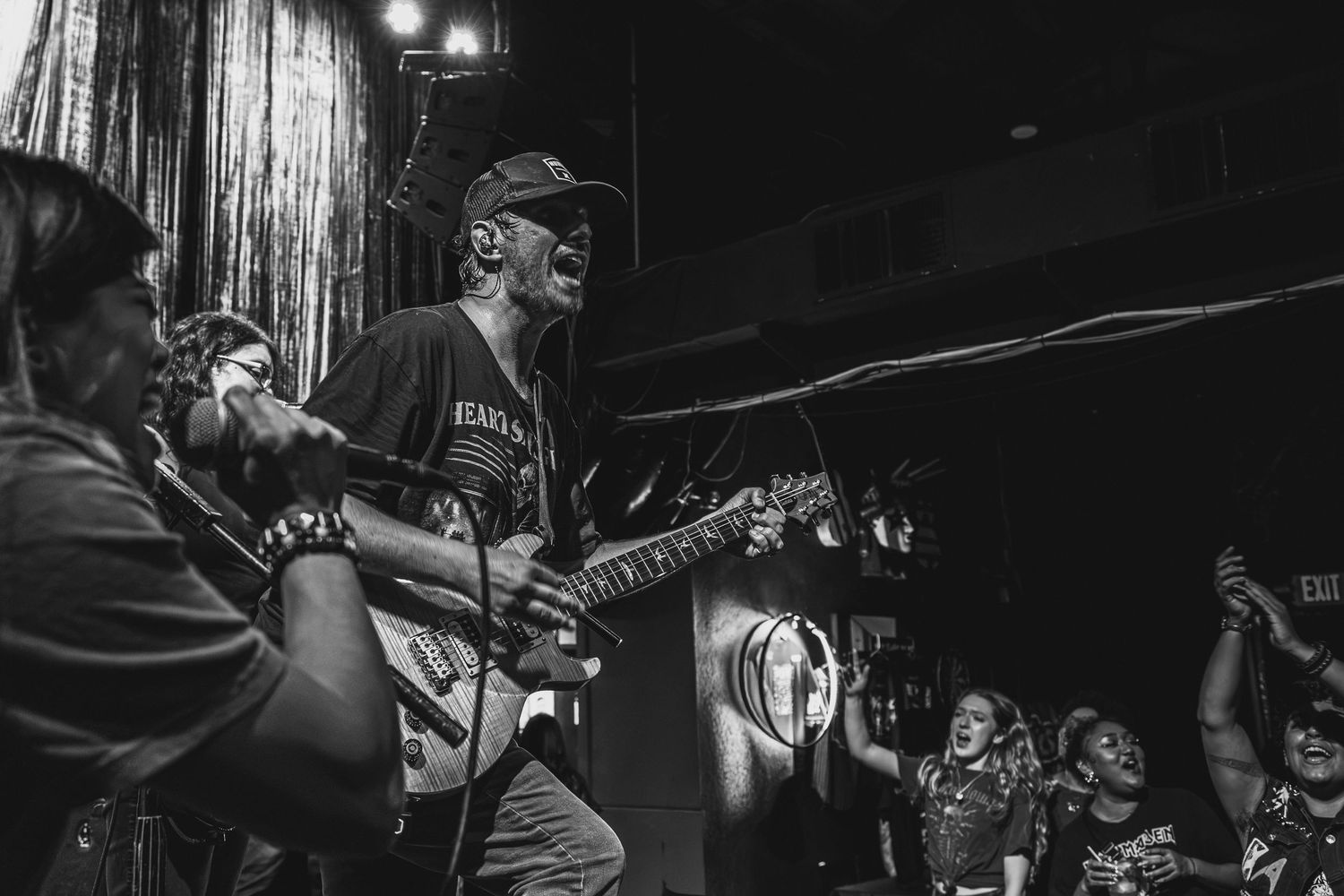 Black and white photo of energetic rock band performing live on stage with guitarist and vocalist under dramatic lighting.