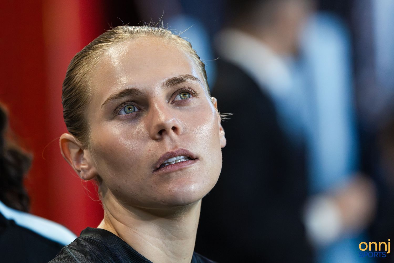 Close-up portrait of a focused female athlete with slicked-back hair at a sporting event.