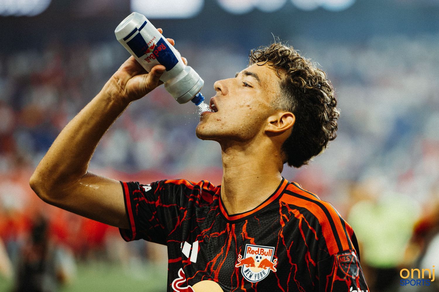Soccer player in red Black jersey drinking water from bottle during match.