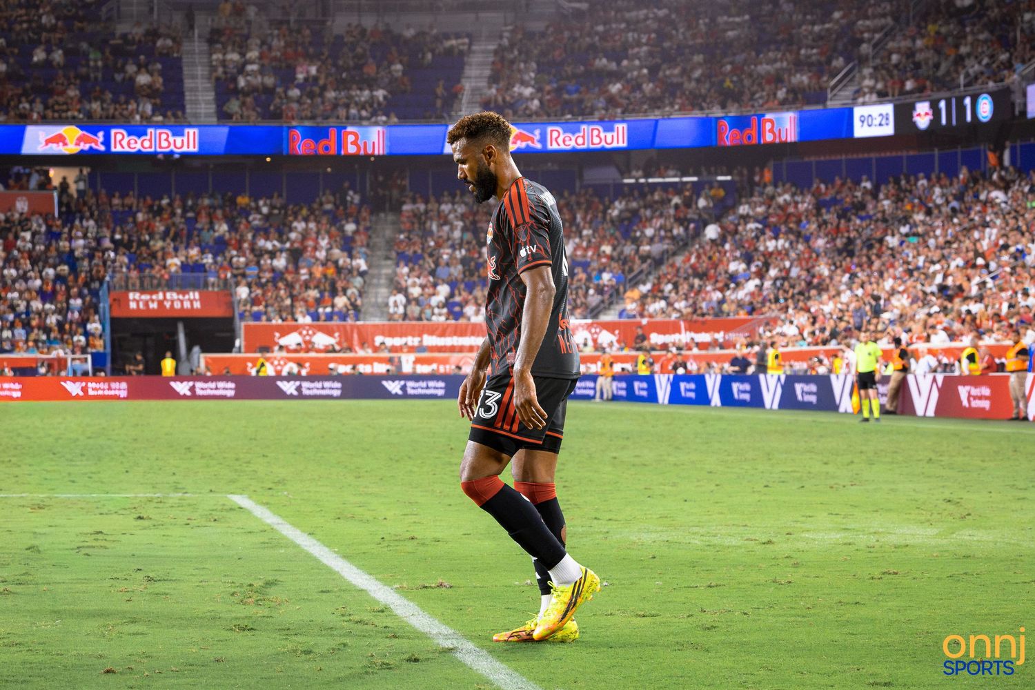 Soccer player in red uniform stands on field during MLS match at Red Bull Arena with crowded stands.