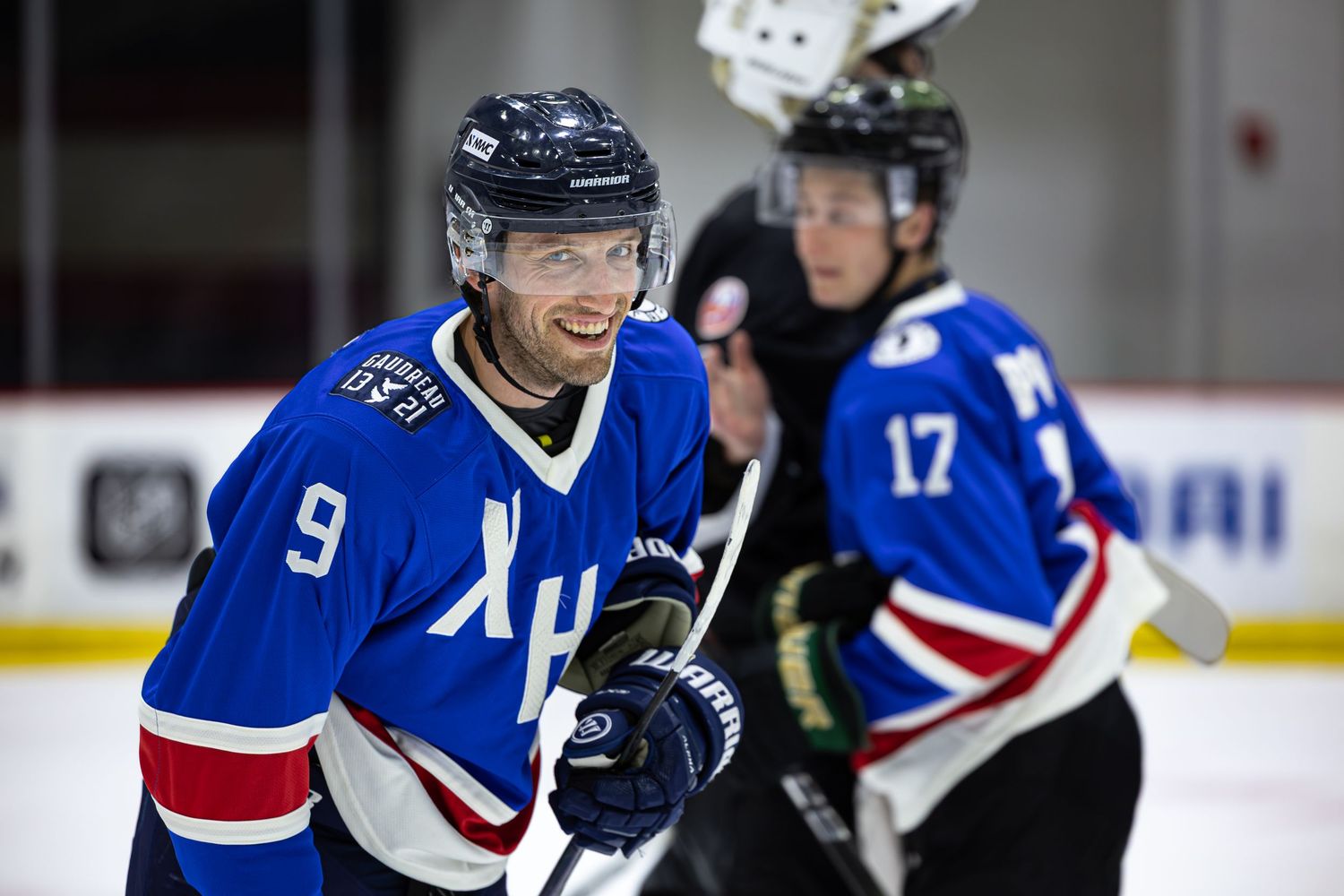 Two ice hockey players in blue jerseys numbered 9 and 17 compete on the rink during a game.