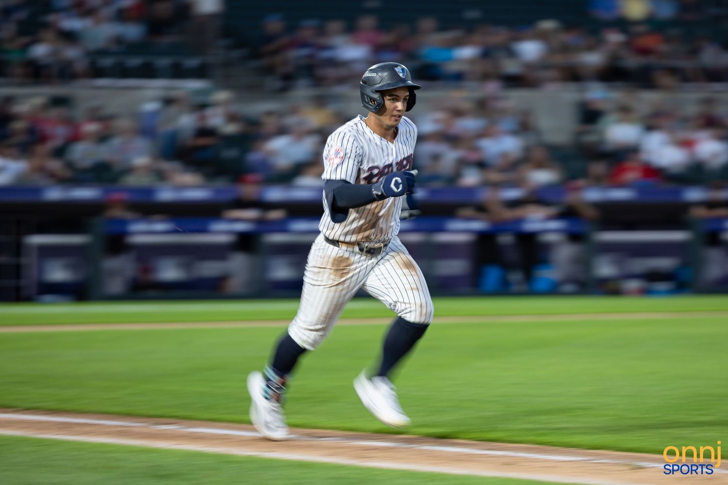 Baseball player in pinstripe Yankees uniform sprints the bases during a night game at the stadium.