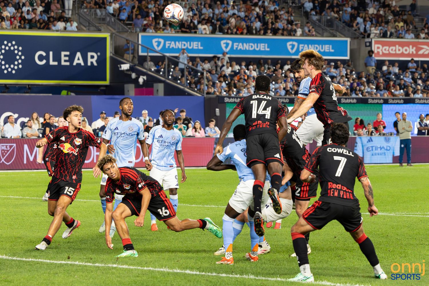 MLS soccer players compete in an intense header duel during a night match with FanDuel and Reebok advertising boards.