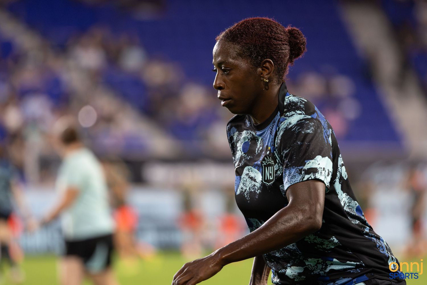 Female soccer player with red hair in dark uniform dribbling on field during a professional match.