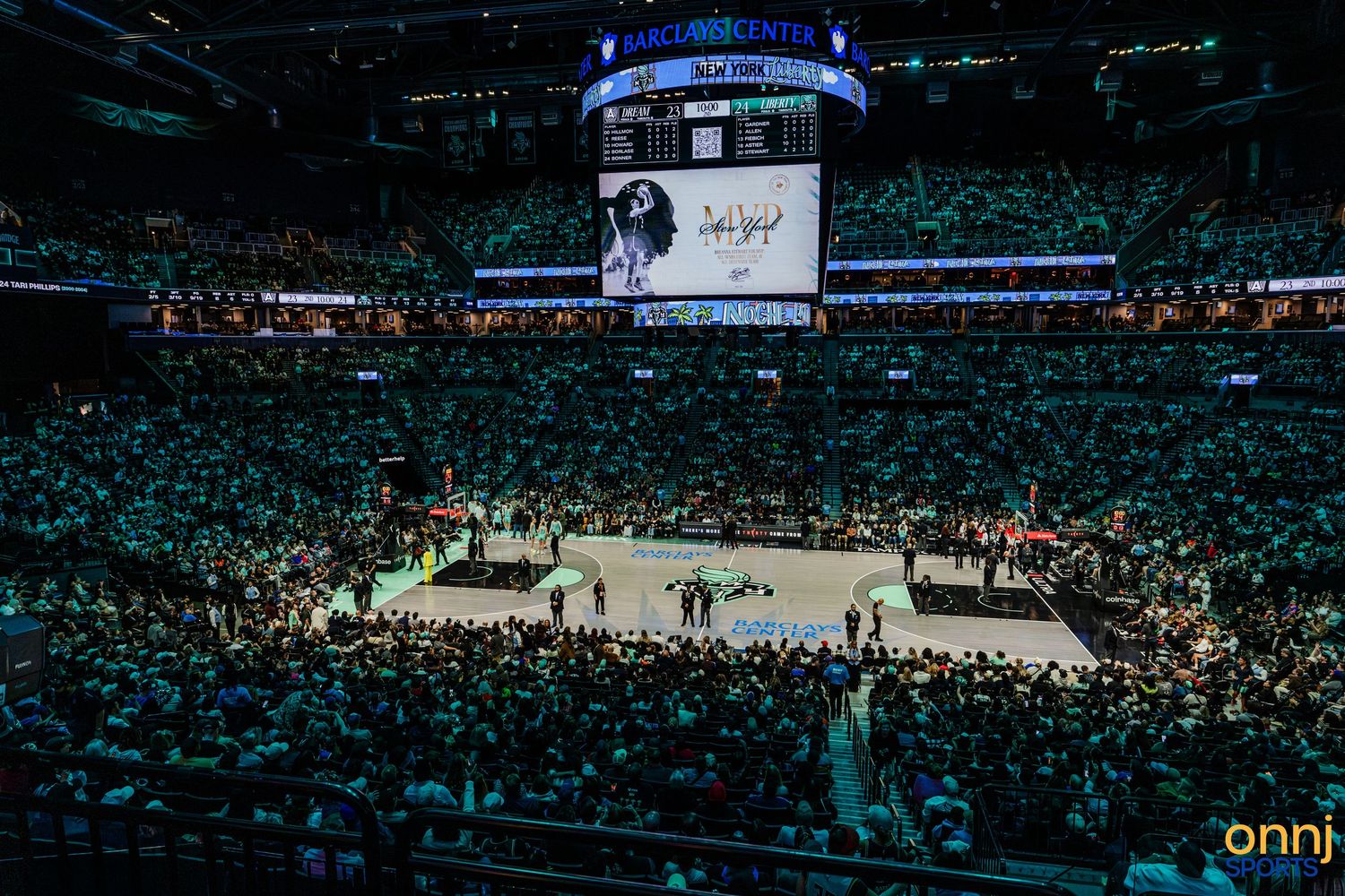 Packed NBA arena with green-lit crowd, large scoreboard, and basketball court during a game at TD Garden.