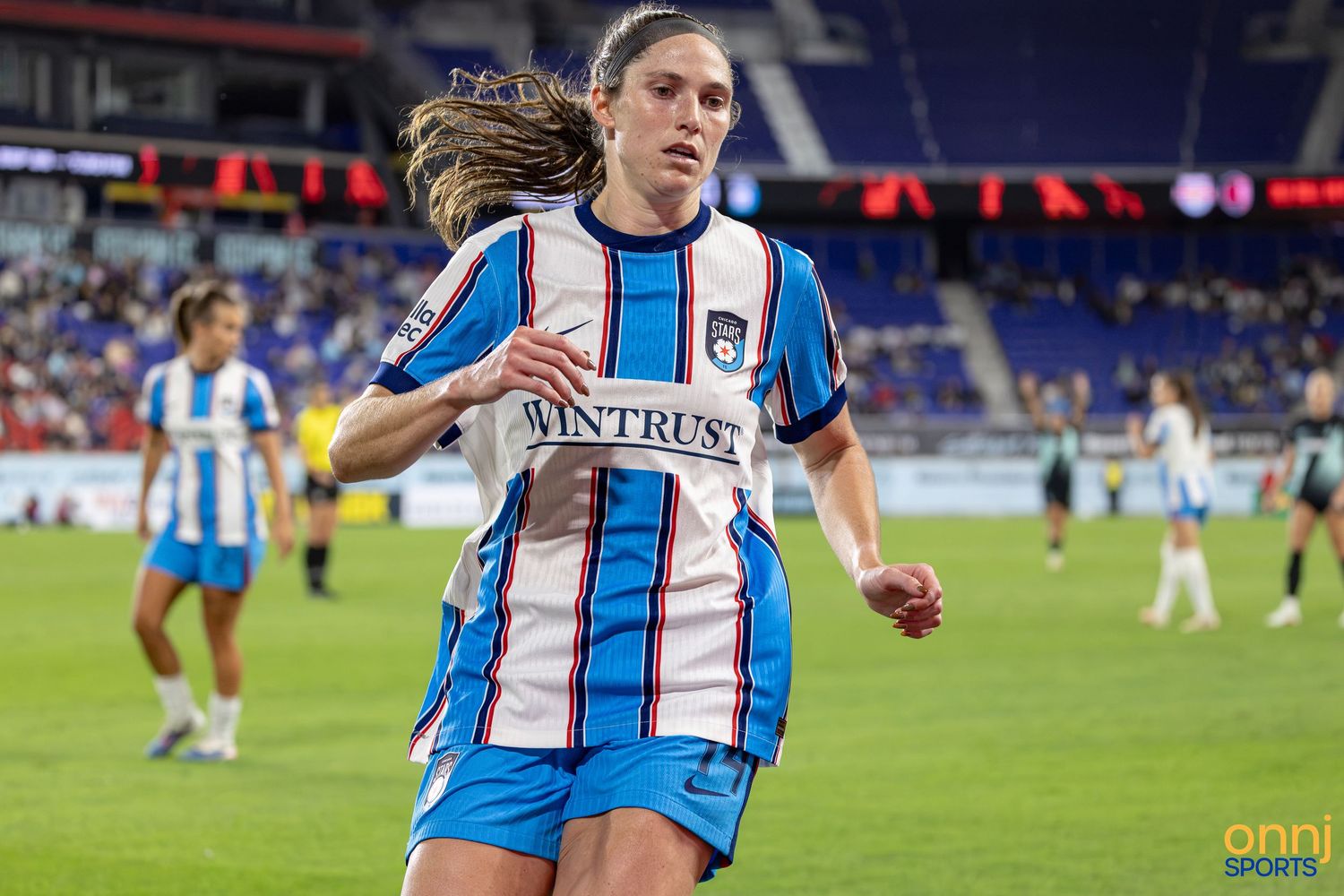 Female soccer player in blue and white striped Wintrust jersey running on field during NWSL match.