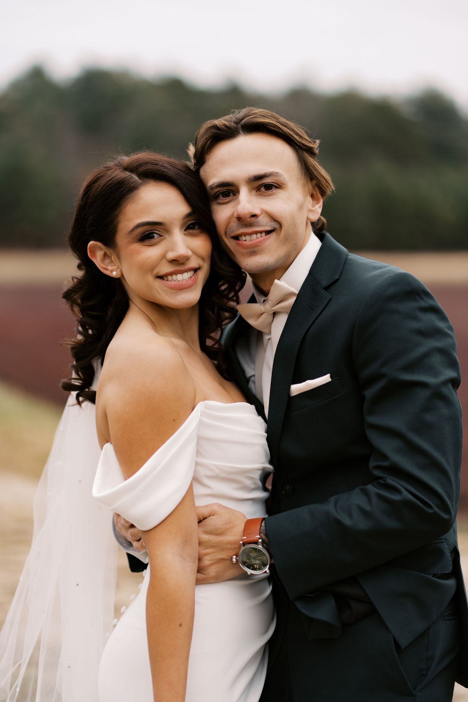 Close-up portrait of a bride and groom smiling together against the deep crimson backdrop of the Rosebrook cranberry bogs in winter.