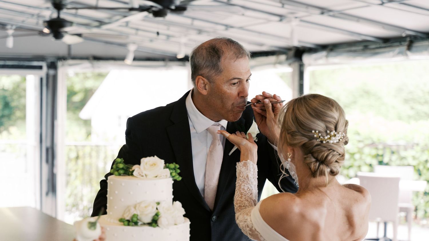 A playful, candid shot of the bride and groom feeding each other cake during their coastal New England wedding celebration.