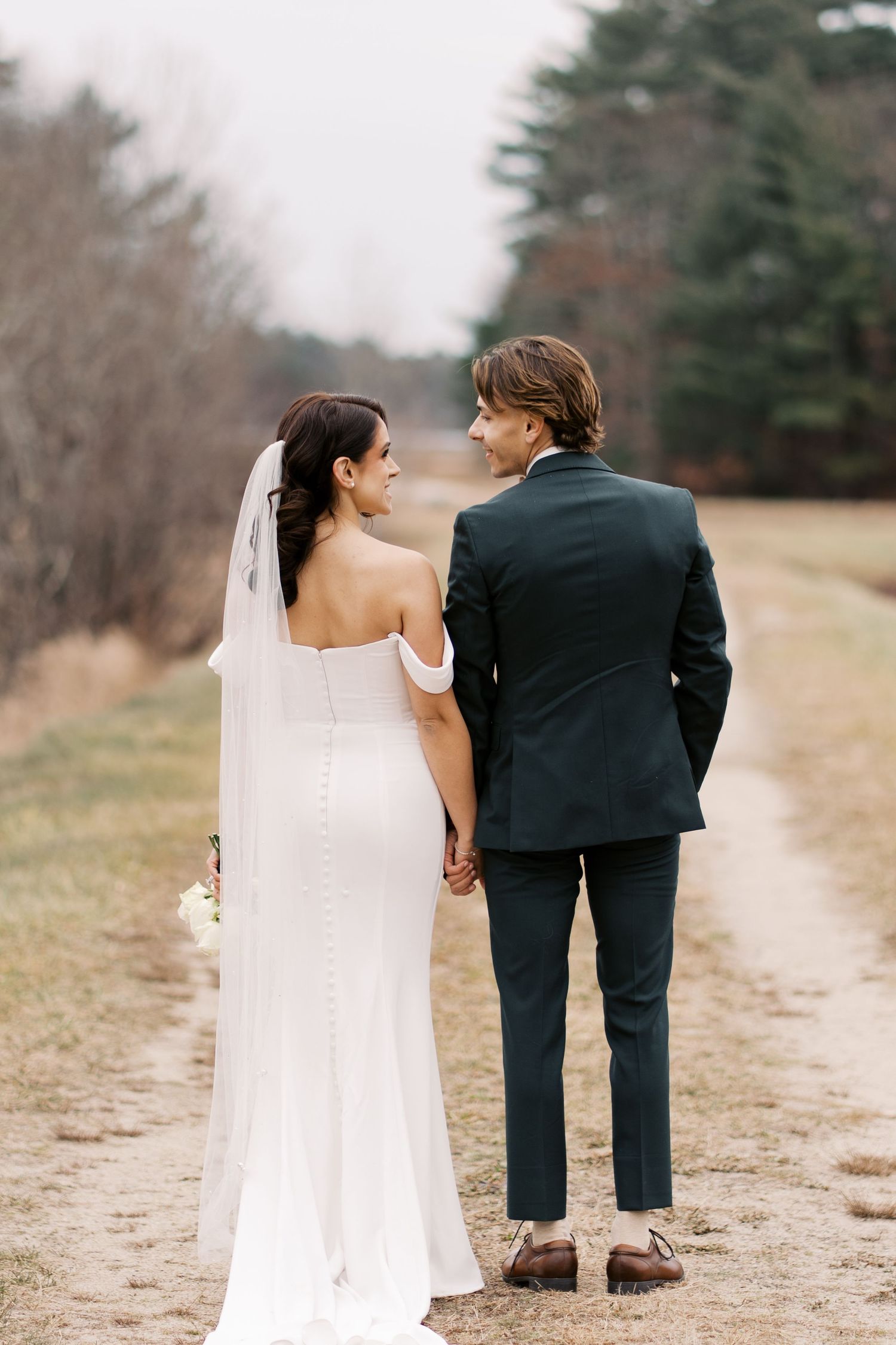 Full-length wedding portrait of a couple walking along a path through the red cranberry bogs at a South Coast winter wedding.