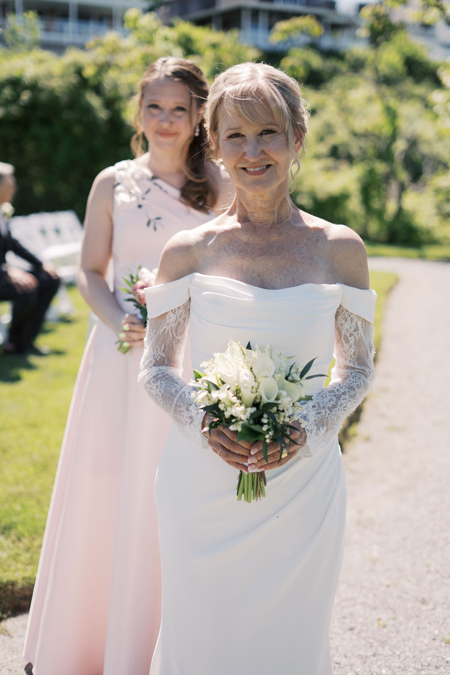 Portrait of a bride in an elegant off-the-shoulder wedding gown standing with her bridesmaid on the lawn at The Boathouse Tiverton.