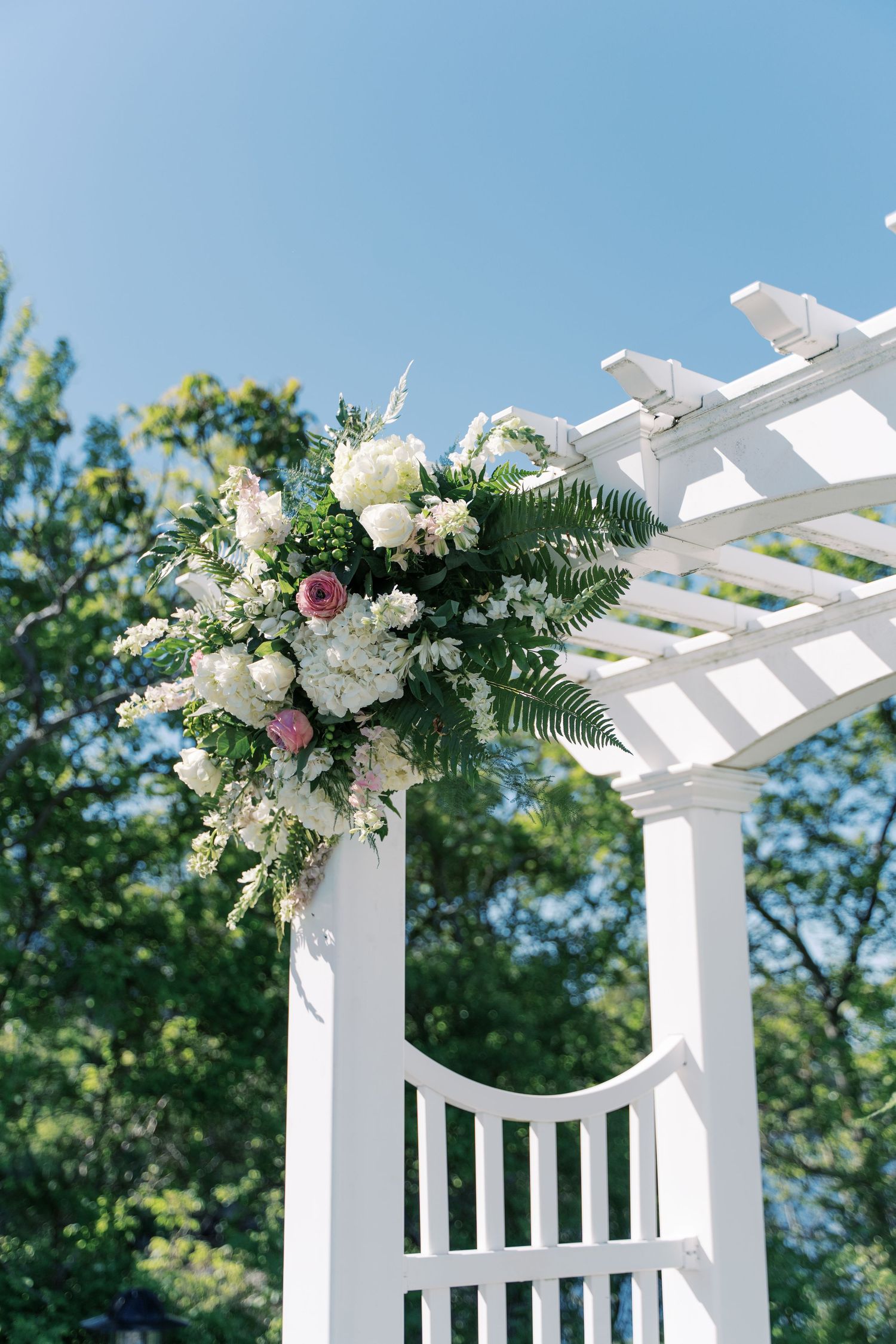 Close-up of a white garden pergola with lush white and pink floral arrangements for a wedding ceremony at The Boathouse Tiverton.