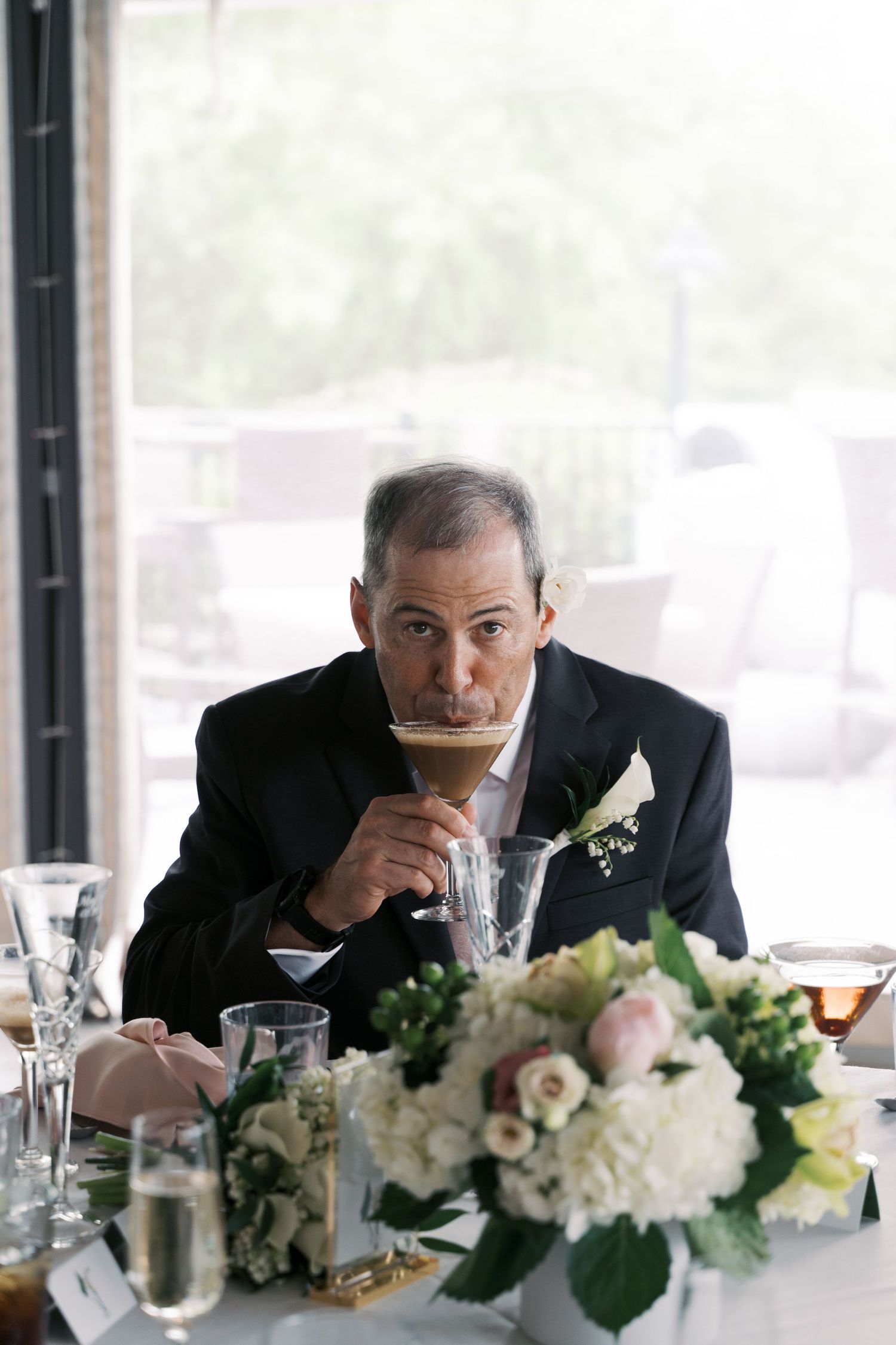 Candid shot of a groom enjoying an espresso martini at his Boathouse Tiverton wedding reception table.