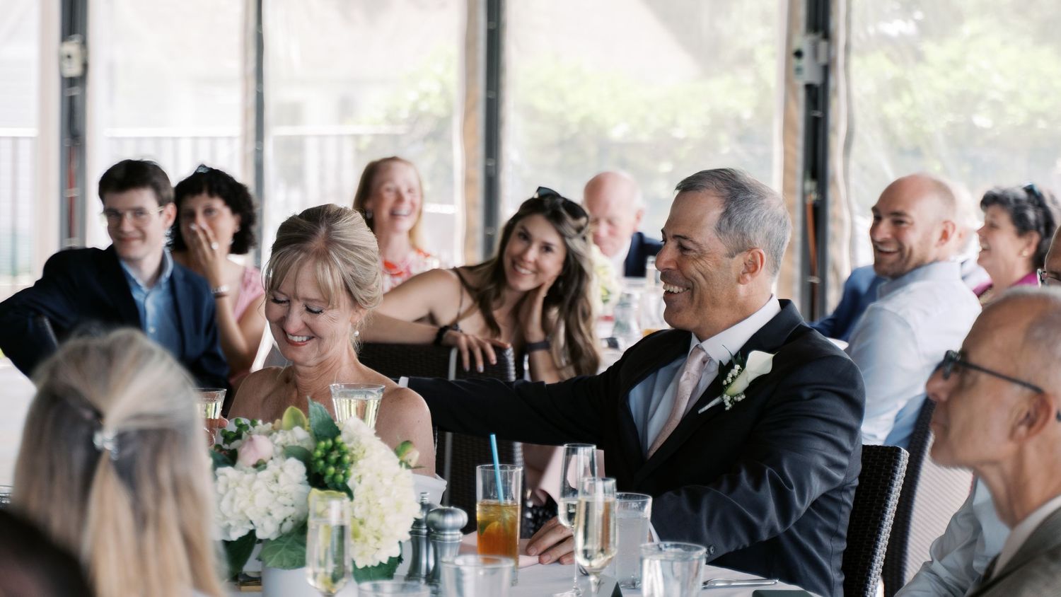A joyful bride and groom laughing with wedding guests during an intimate reception dinner at The Boathouse in Tiverton, RI.