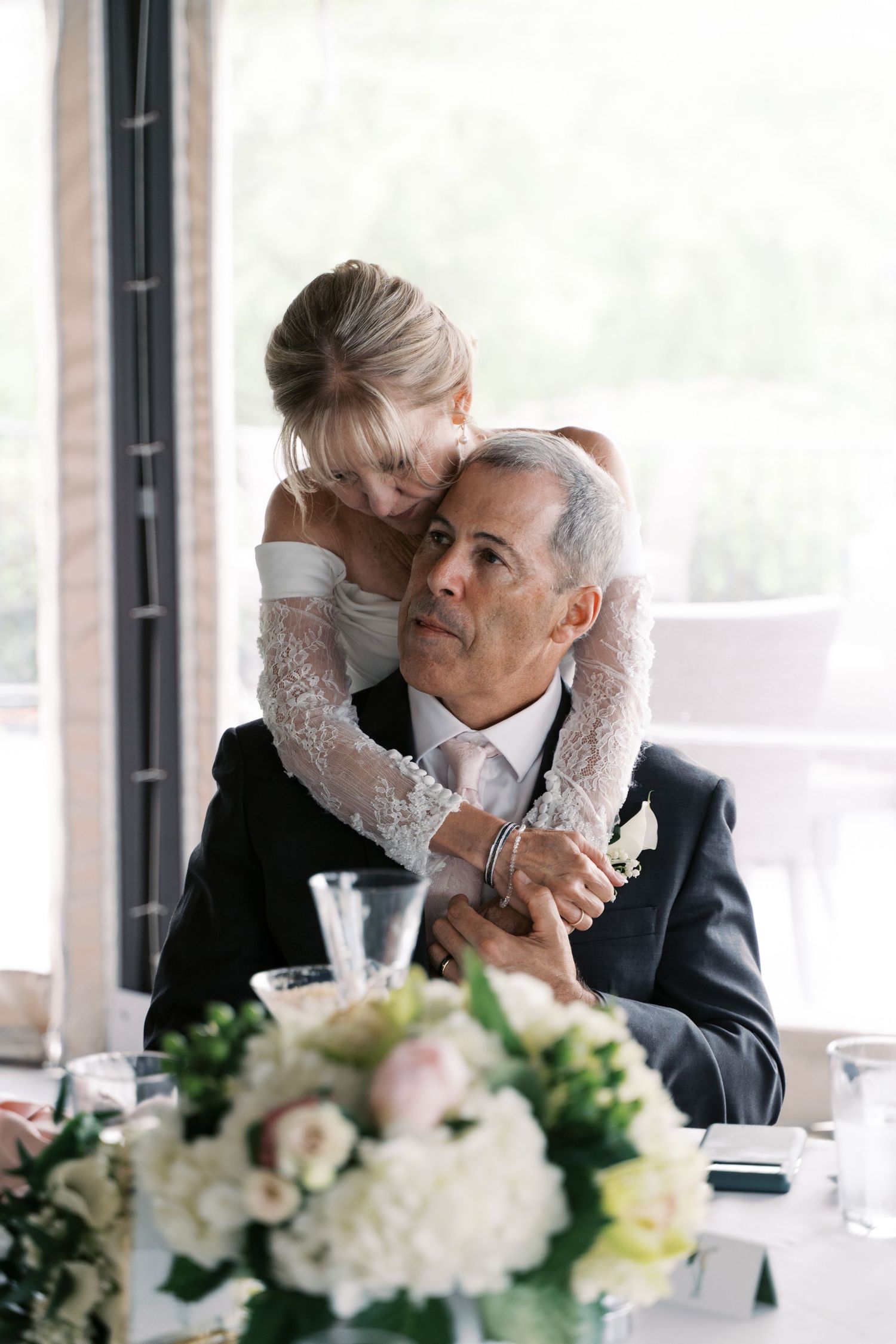 An emotional, candid moment of a bride embracing her groom from behind during wedding toasts in Tiverton.