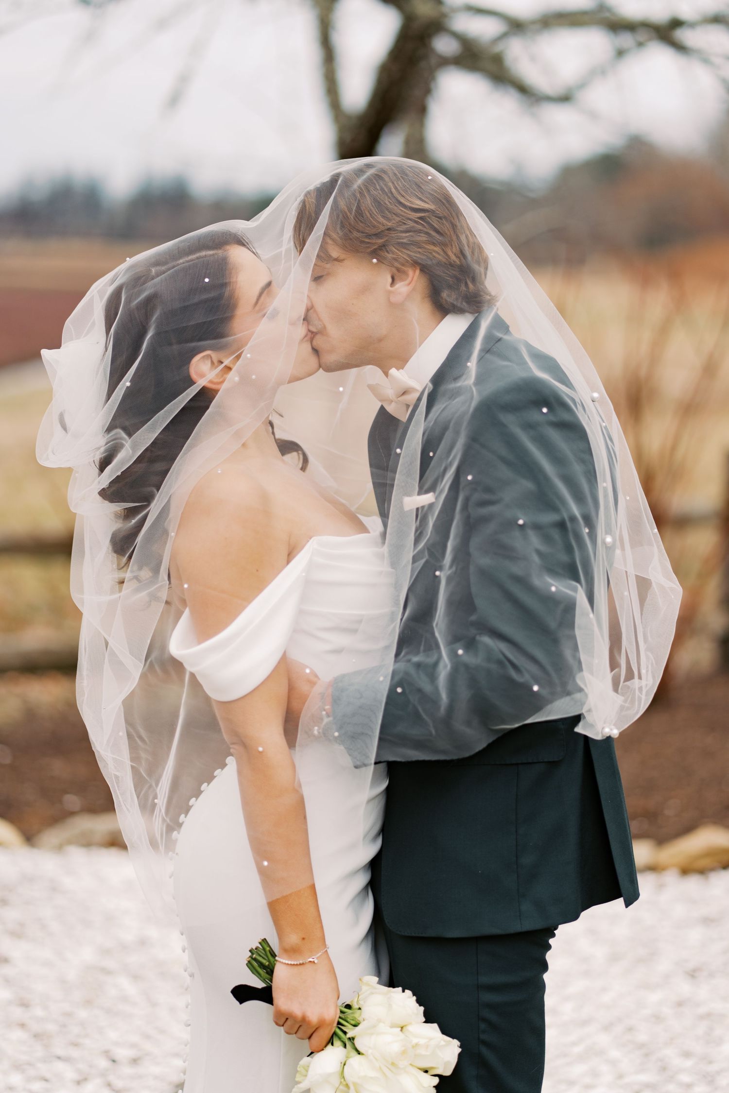Romantic wedding portrait of a couple kissing under a sheer bridal veil during a winter sunset in Wareham, MA.