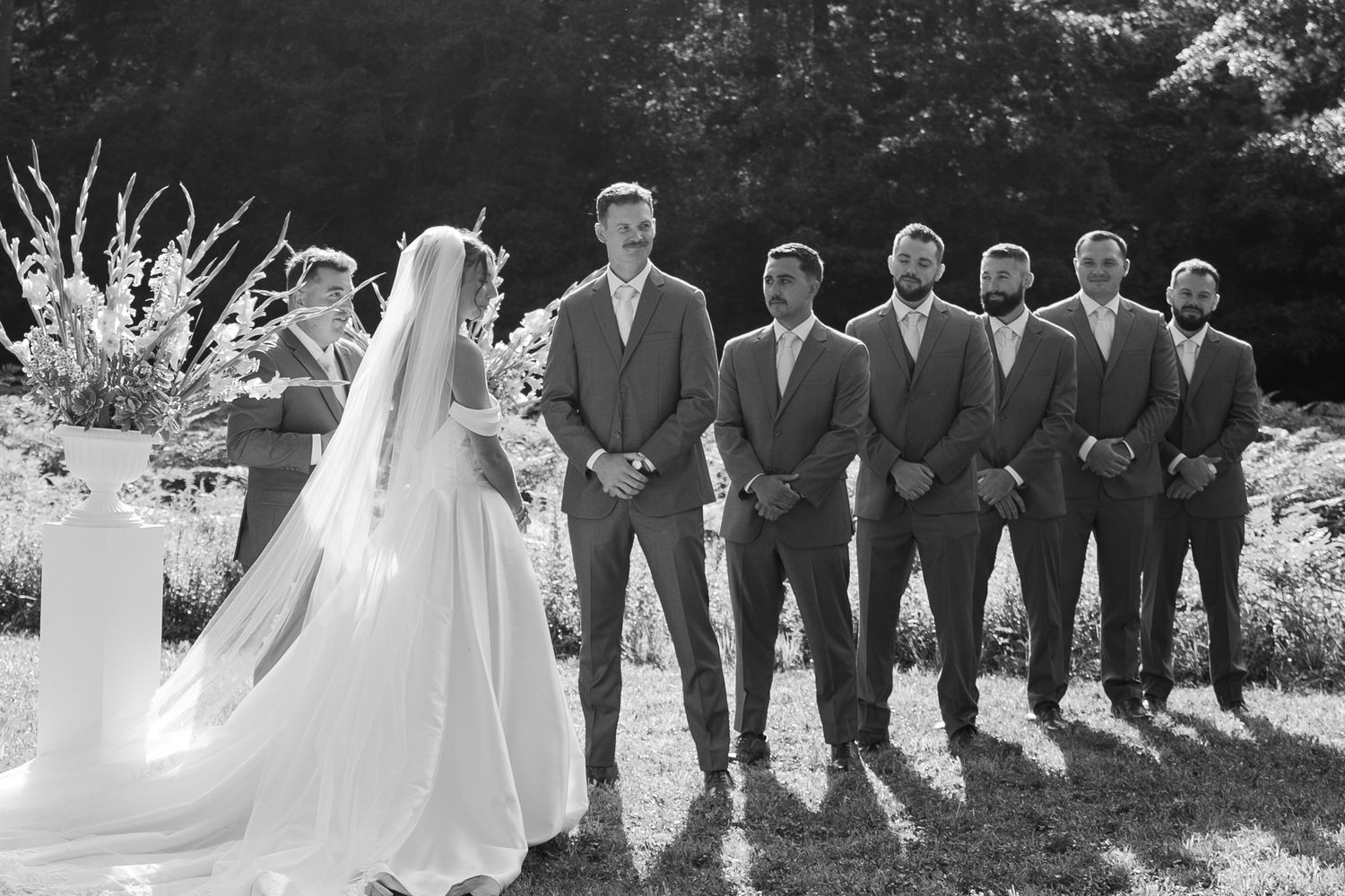 Black and white photography of a wedding ceremony at Salt River Farm, capturing the groom and his groomsmen in slate blue suits.