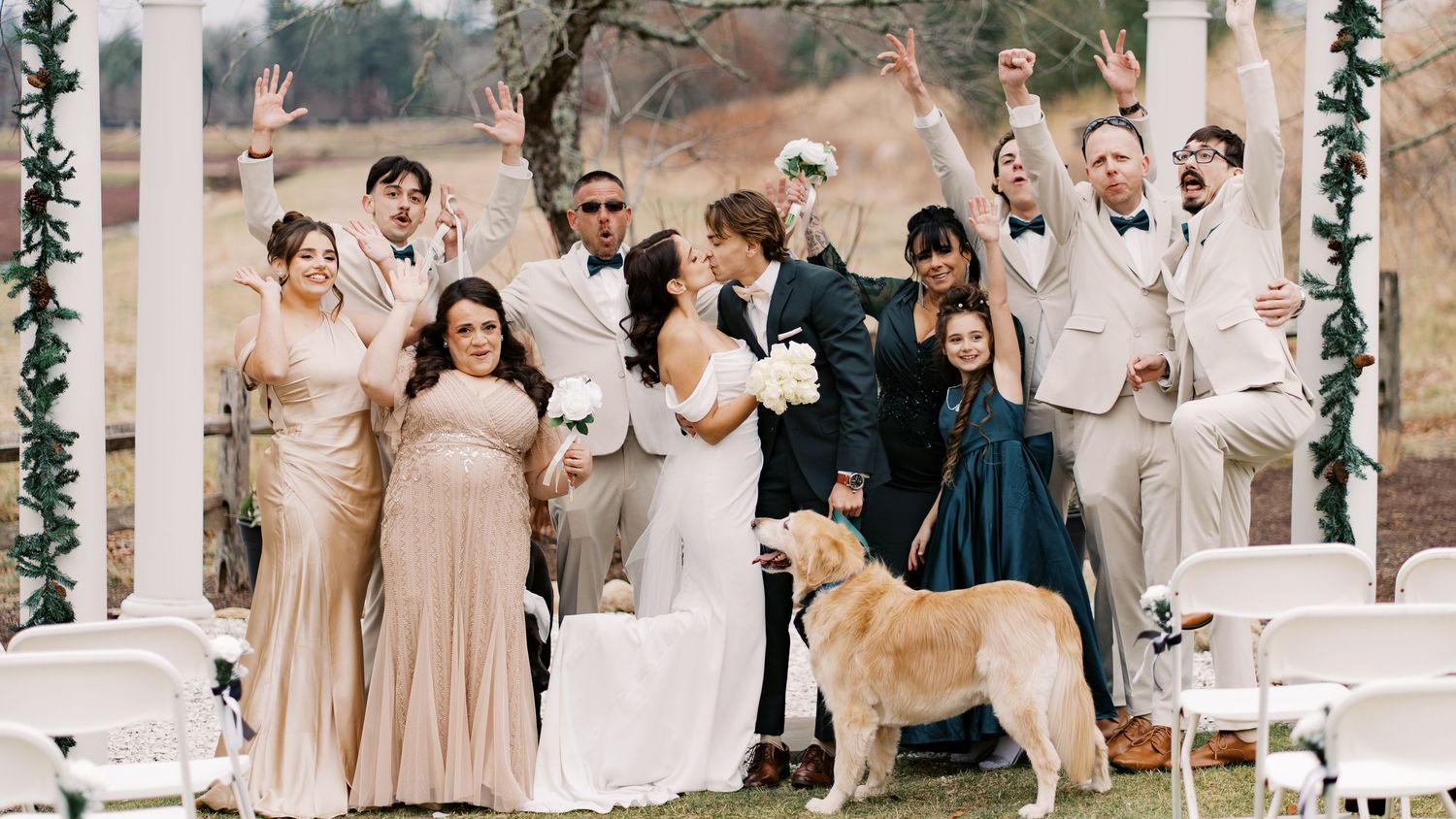 A joyful wedding party posing with a golden retriever under a white garden arbor at Rosebrook Event Center during a celebration in Wareham.