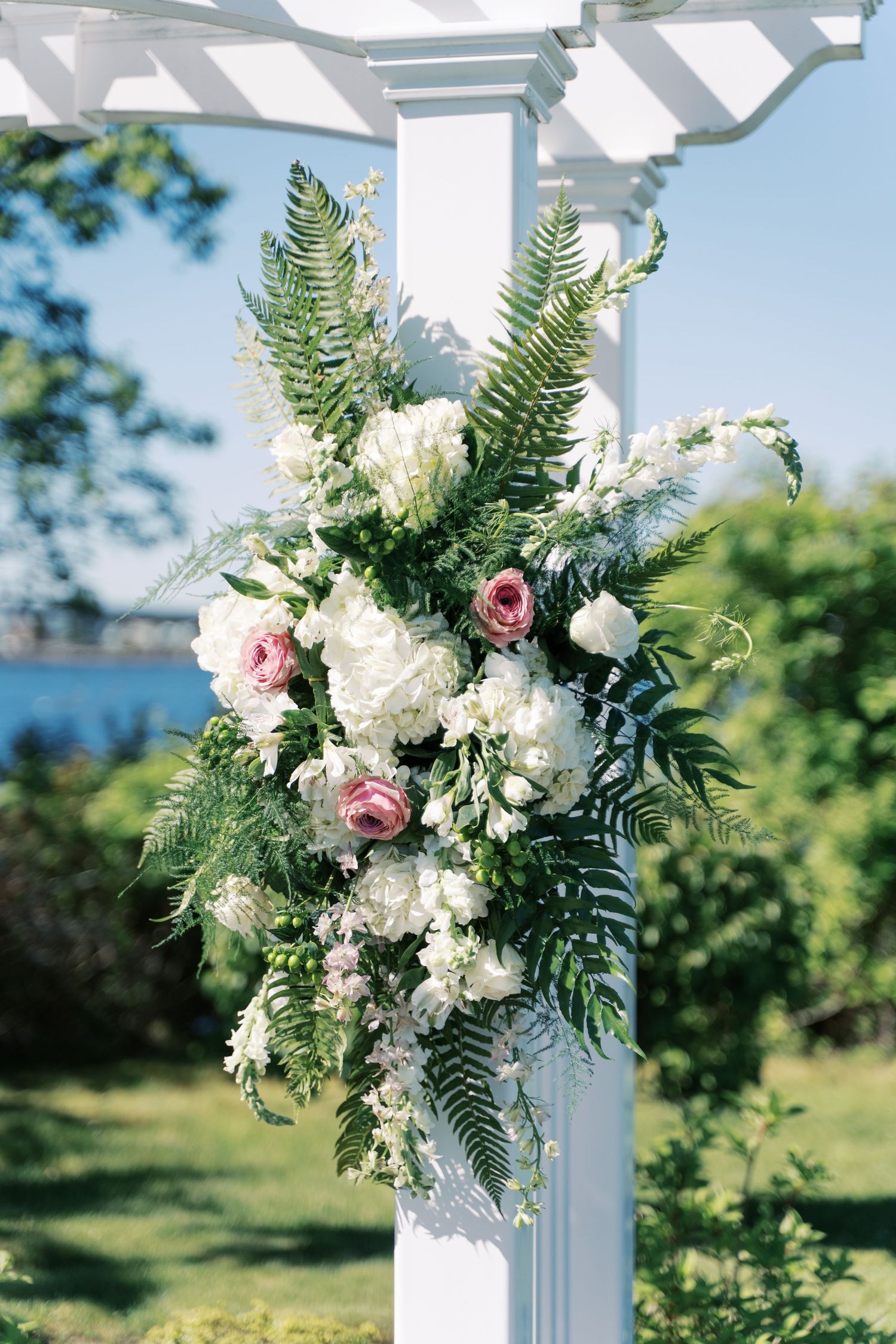 Close-up of a romantic wedding floral arrangement with pink roses, white hydrangeas, and greenery on a white pergola.