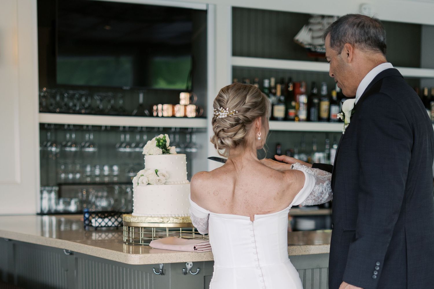 Wedding cake cutting moment at the Boathouse bar, featuring a minimalist white tiered cake and coastal interior decor.
