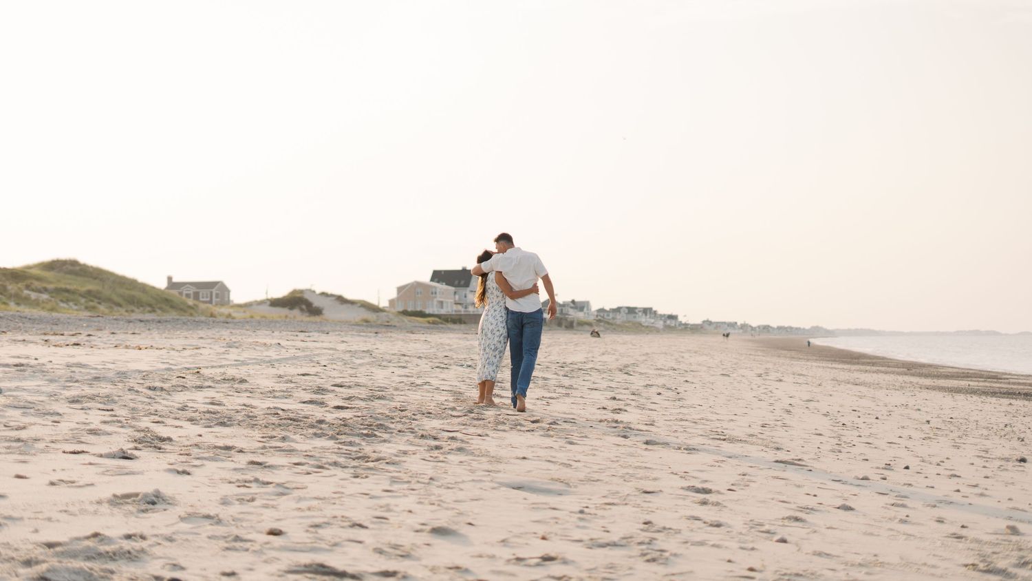 Couple holding eachother and walking down the beach during golden hour at Rexhame Beach in Marshfield, MA.