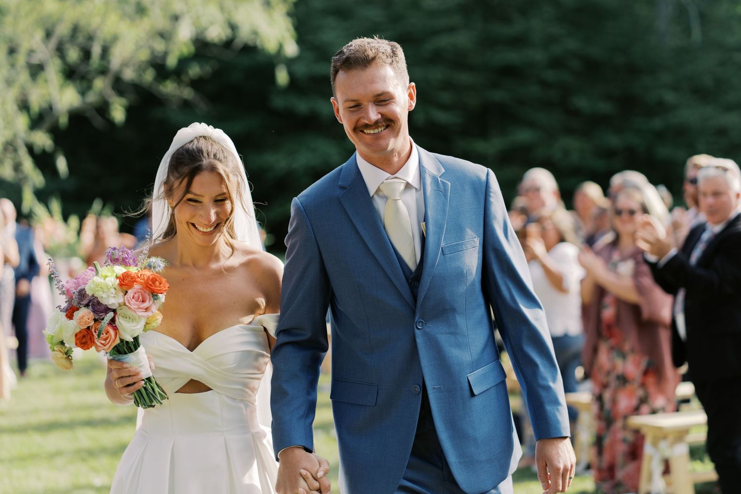Joyful bride and groom walking down the aisle together after their Marshfield barn wedding ceremony during golden hour.