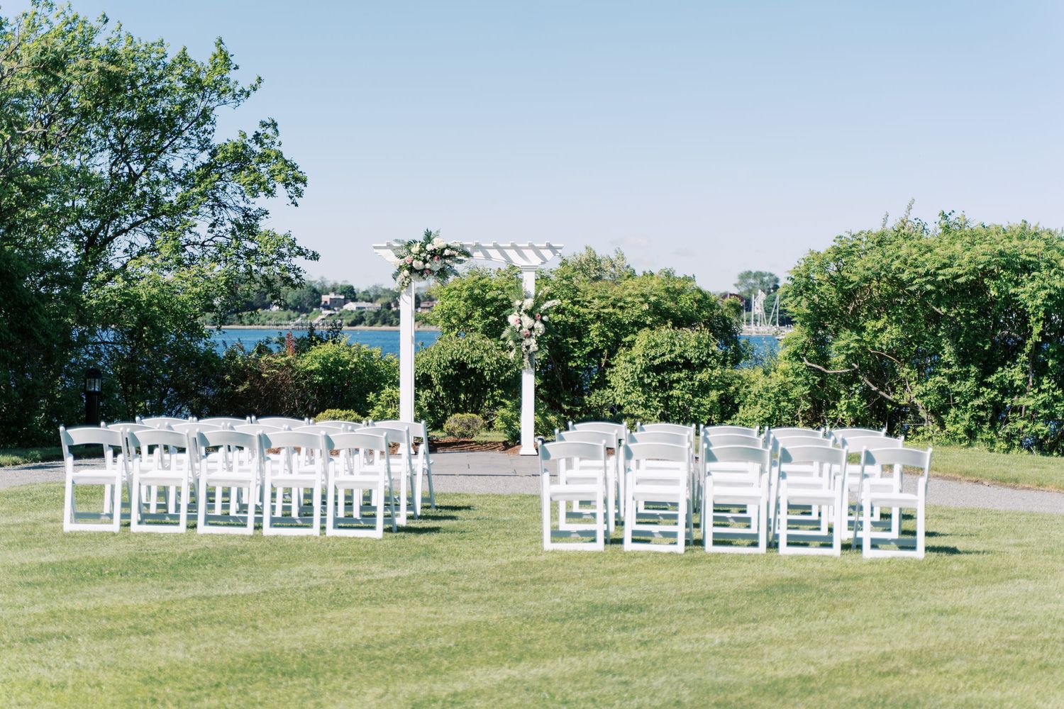 Wide angle view of a coastal wedding ceremony at The Boathouse in Tiverton RI overlooking the Sakonnet River at sunset.