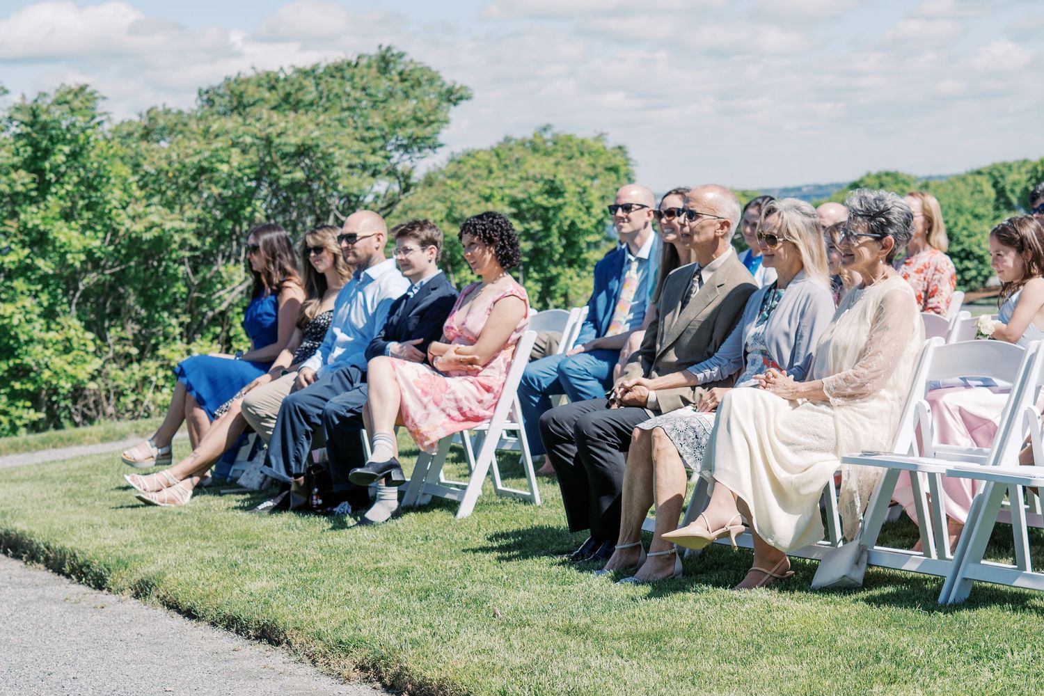 Rows of wedding guests seated in white chairs on the lawn at The Boathouse Tiverton during a sunny afternoon ceremony.