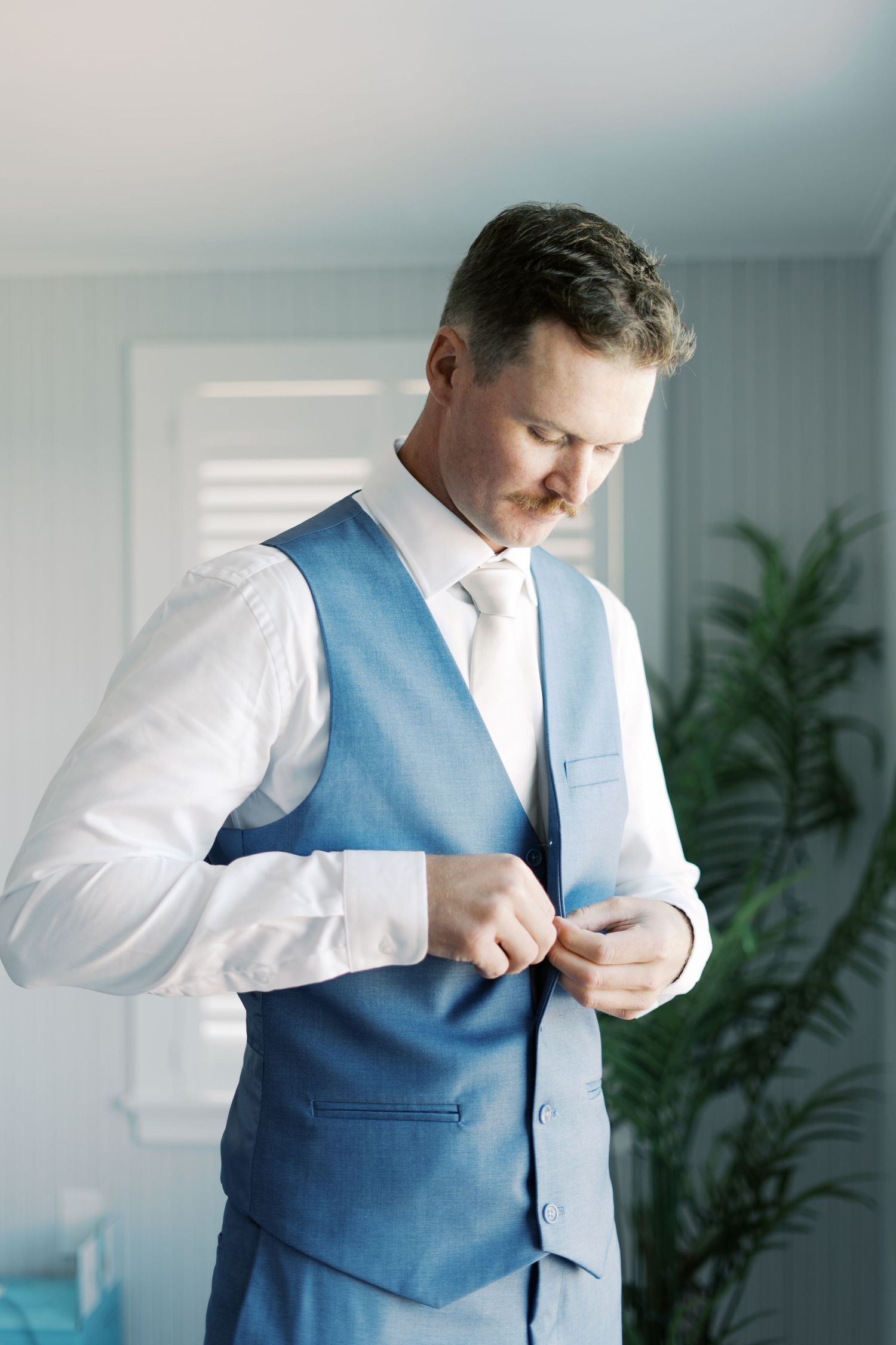 Groom in a slate blue suit adjusting his vest for a summer afternoon wedding at Salt River Farm.